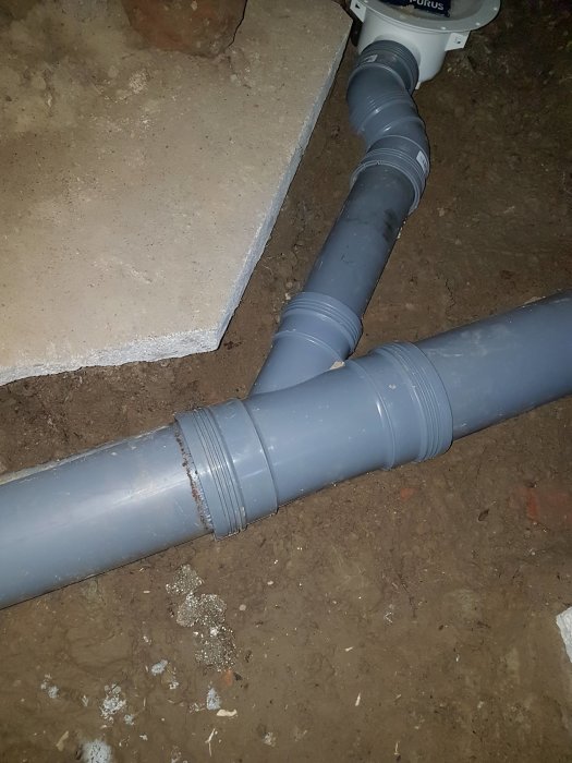 Nyinstallerat grått avloppsrör på fuktig källargrund bredvid gammalt betonggolv.