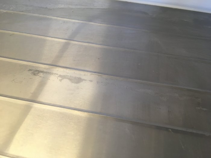 Fläckar och missfärgningar på en rostfri diskbänks yta där en bänkdiskmaskin har stått.