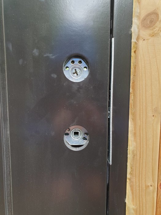 Svart garagedörr med förberedda hål för cylinderlås och handtag, utan monterat beslag.