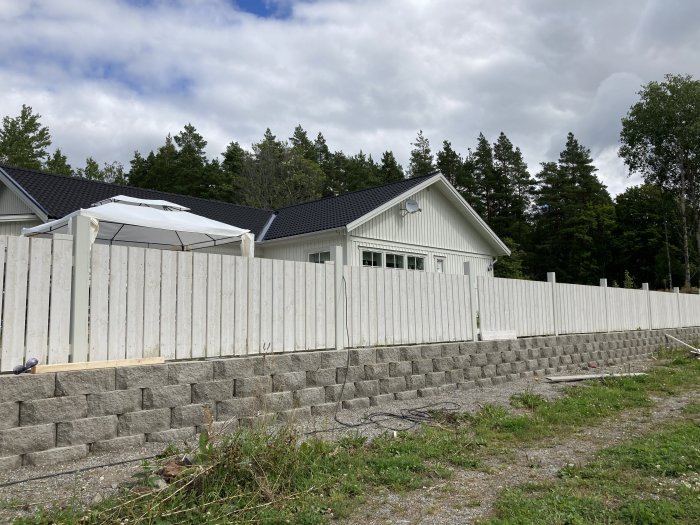 Nybyggt staket med vita spjälor uppsatta på en grå stödmur vid ett enfamiljshus.