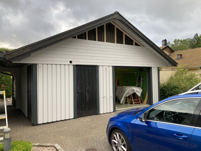 Ny panel monterad på en carport med öppen verkstadsdel och en blå bil framför.