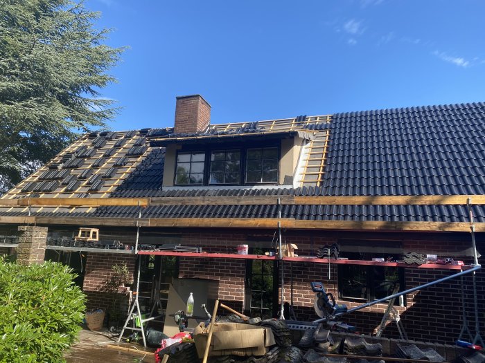Tak under renovering med nya svarta pannor, delvis lagt, med synlig skorsten och takfönster.