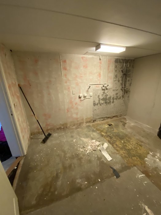 En renoverad tvättstuga med rivna väggar, våtrumsmatta uppdragen och limrester synliga på golvet.