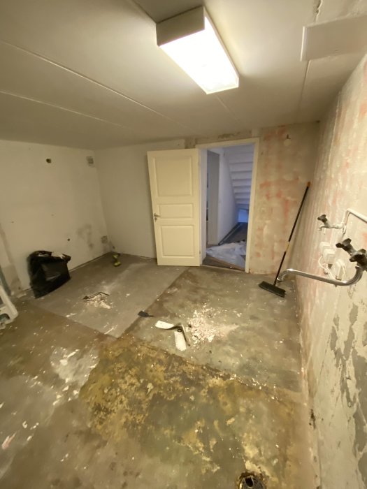 Ruffigt tvättstugerum under renovering med rester av lim efter borttagen plastmatta på betonggolvet.