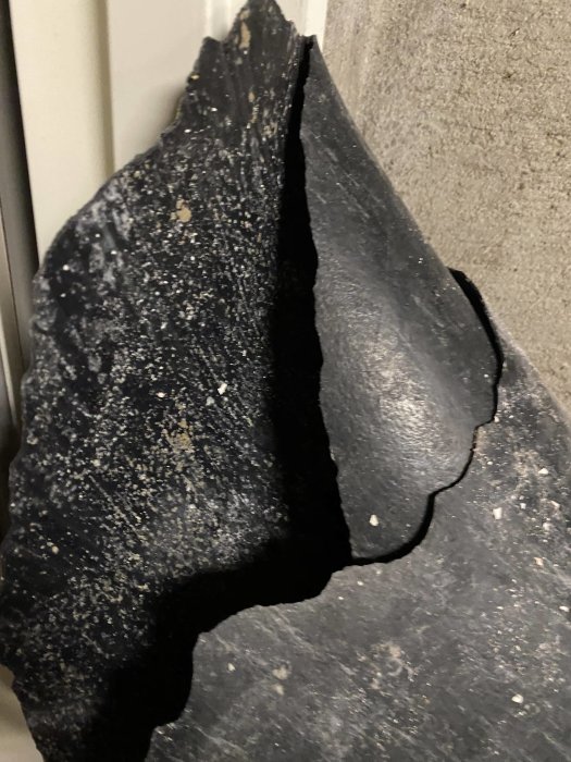 Skadad asfaltbit med sprickor hållen upp framför en betongvägg.