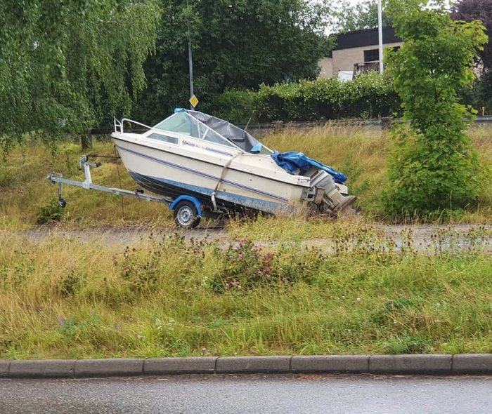 En övergiven båt på en trailer vid vägkanten, nedklottrad och delvis täckt med en blå presenning.