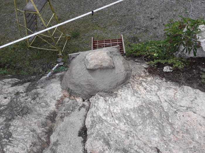 Två betongplintar gjutna på en klippa med sten och verktyg i bakgrunden.