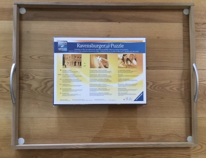 Hemtillverkad pusselram i trä på ett trägolv med ett Ravensburger pusselpaket inuti.