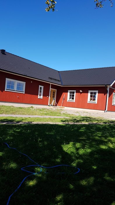 Ett svenskt rött hus med vita knutar och öppen dörr under solig himmel.