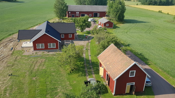 Flygbild av en lantgård med röda hus, gröna fält i bakgrunden och en grusväg.