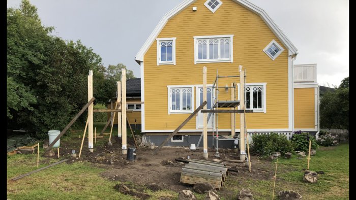 Uppställda 140x135mm limträstolpar för byggprojekt med urjackning, framför ett gult hus, planeringsfas med osäkert takvinkel och golvnivå.