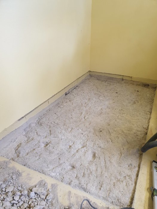 Ojämnt betonggolv med rester av bilning och synliga stenar i ett gammalt pannrum.