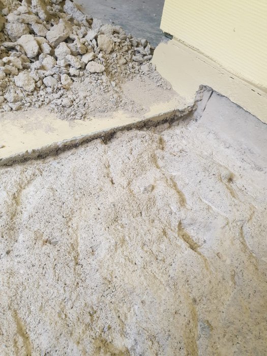 Ojämnt bilat golv med olika stora stenar och höjdskillnader bredvid en intakt betongplatta.