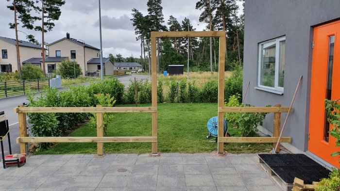 Obehandlat trästaket med en pergola över grindområdet under konstruktion framför ett hus.