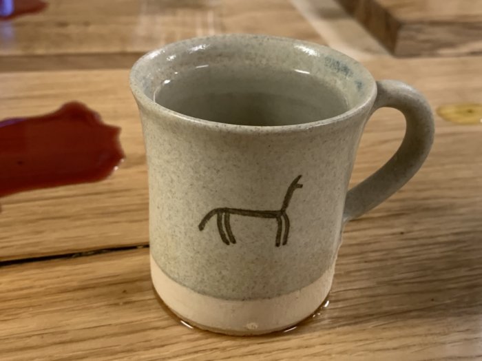 Stengodsmugg med enkelt djurmotiv på träyta med kaffefläck och vattenringar runtomkring.
