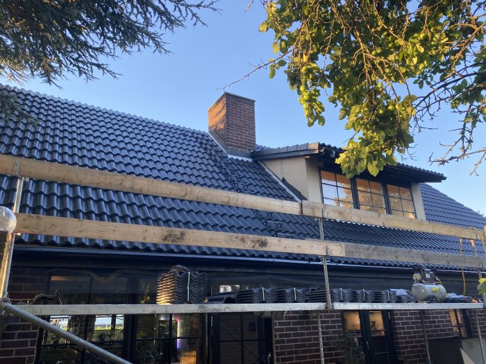 Renoverat tak på hus med ny svarta takpannor och välintegrerade gavelpannor, omgiven av natur och ställningar.
