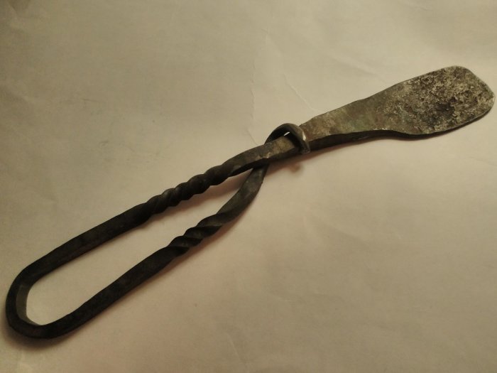Smedsarbete av ett tängerformad objekt med handtag i spiral och platt ände.