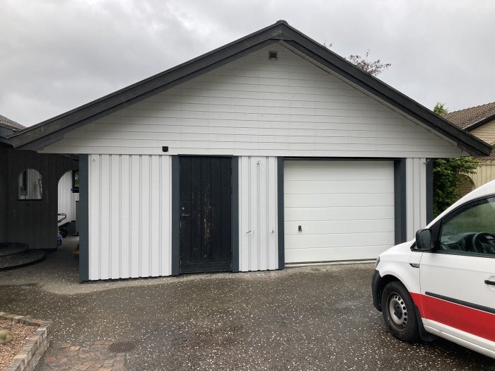 Nyrenoverad vit garagebyggnad med svart dörr och parkerad vit bil framför.