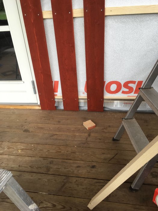 Delvis renoverad vägg med rödmålad panel och oskyddad isolering vid golvet.