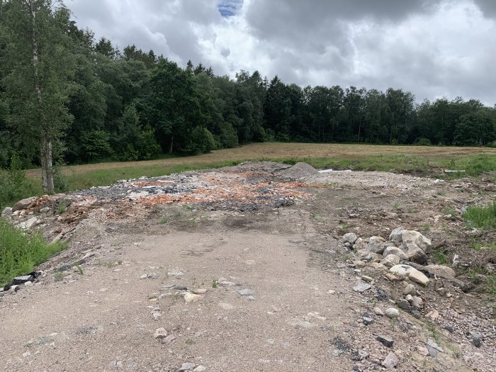 Förberett område för bygge med borttaget material och synlig dränering i ett naturligt landskap.