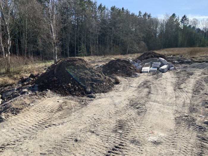 Jordhögar och betongblock på en grävd byggplats med träd i bakgrunden.