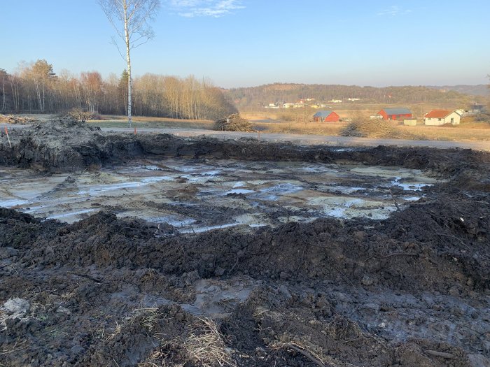 Uppgrävd mark med synlig dränering förberedd för byggande av hus, med landskap i bakgrunden.