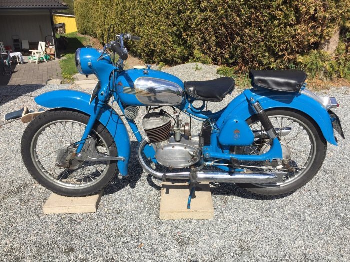 Blå veteranmotorcykel parkerad utomhus, troligen en modell från 1960-talet.