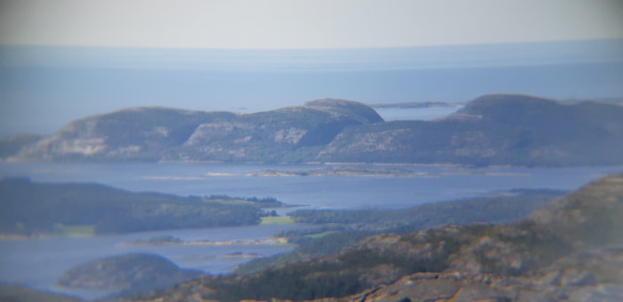 Utsikt över dimmiga berg och en sjö med grönskande träd i förgrunden, tagen genom ett suddigt linsfilter.