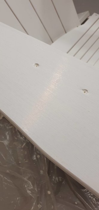 Vitmålat träplank med synliga penseldrag och skruvhål efter 28 timmar torkning.