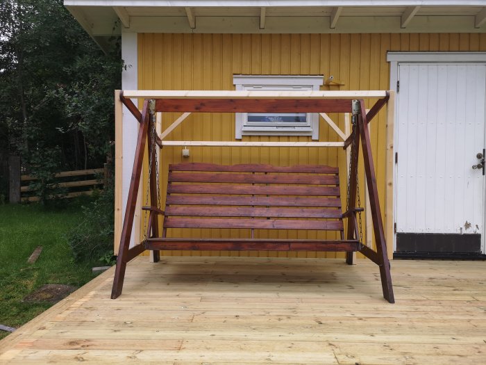 Hammock med träram utan tak framför ett gult hus, redo för installation av nytt plasttak.