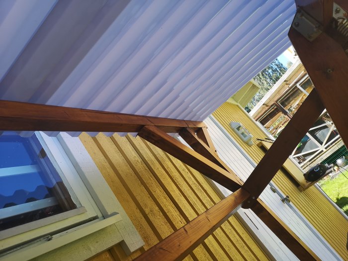 Ombyggd hammock med nytt permanent plasttak och nya träreglar för lutning mot en gul husvägg.