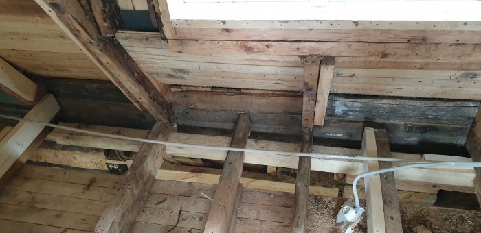 Vy ovanifrån av en 5 meter lång träbalk som stödjer golvbjälklag och takstolar i en byggkonstruktion.