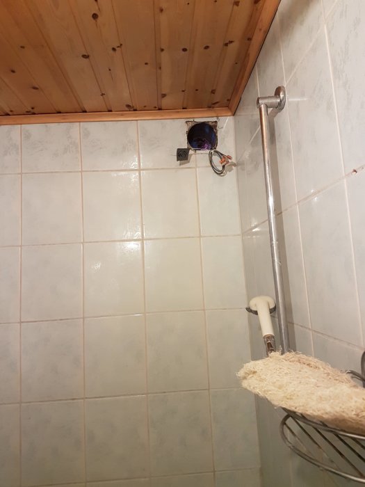 Elektriska kablar och öppning efter borttagen fläkt i badrum med kakelväggar och träpanel i taket.