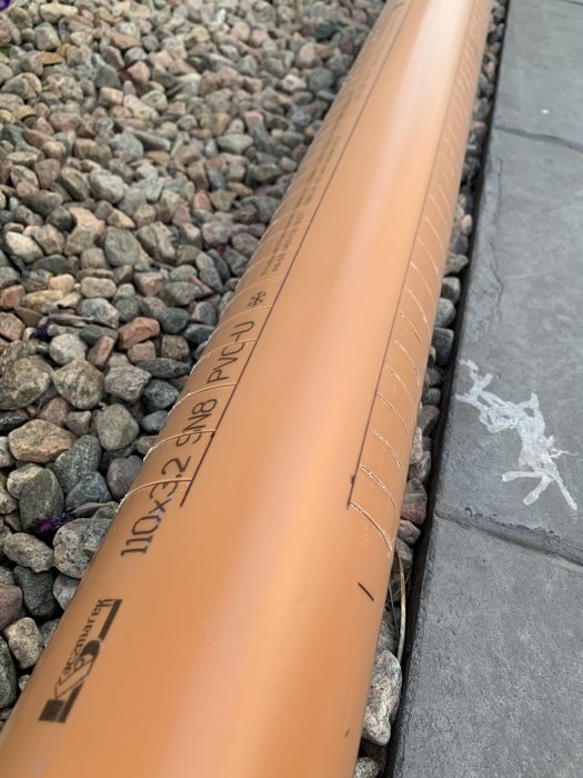 Orange PVC-rör med uppmärkta och inslitsade sektioner redo för montering av markduk.