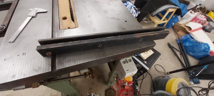Sågbord med justerbart anhåll och begränsad klyvbredd på en verkstadsbakgrund med verktyg och röra.