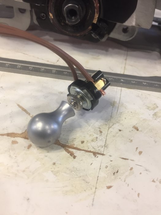 Gammal dragbrytare monterad på en arbetsyta med synlig kabel och en del av verktyget i bakgrunden.