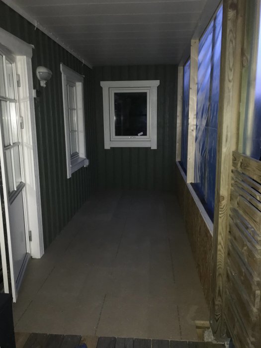 Inomhusvy av ett renoveringsprojekt med delvist oskyddade fönster och synlig golvspån.