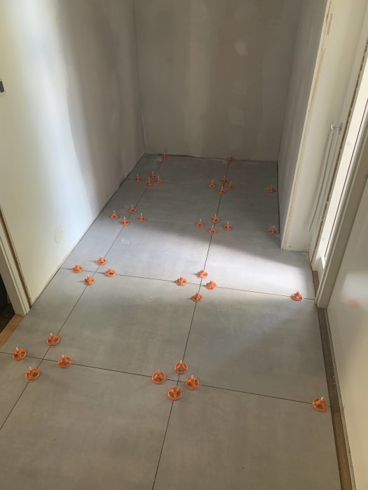 Renoveringsprocess av en hall med nytt klinkergolv som läggs, synliga avståndshållare mellan plattorna.