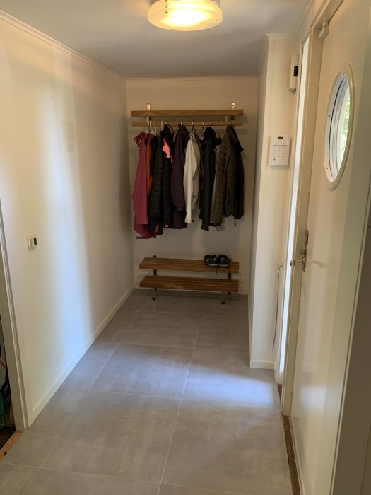 Renoverad hall med klädhängare, bänk, nytt golv och ljus väggpanel.