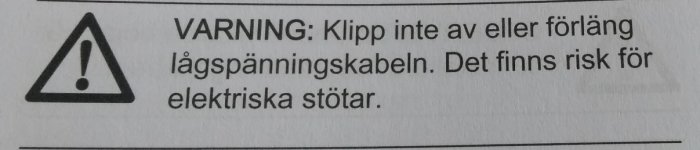 Varningsskylt som instruerar att inte klippa av eller förlänga lågspänningskabel på grund av risk för elektriska stötar.