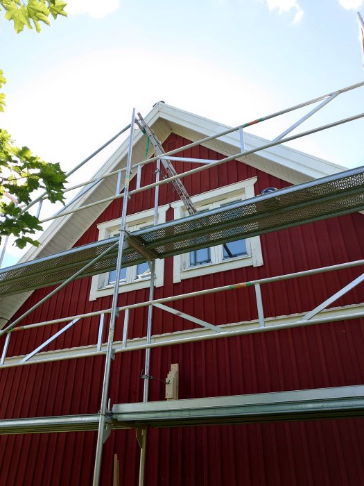 Stegar osäkert fästade vid en byggnadsställning vid ett rött hus, riskabel konstruktion.