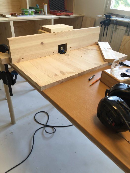 Hemmagjord fräsarbänk med upp och nervänd fräs monterad i ett urtaget bord, omgiven av träkonstruktioner.