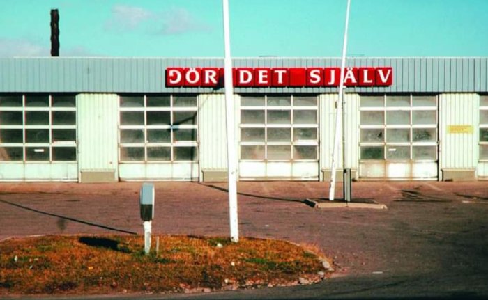 Byggnad med skylt där det står 'GÖR DET SJÄLV' mot en klarblå himmel.