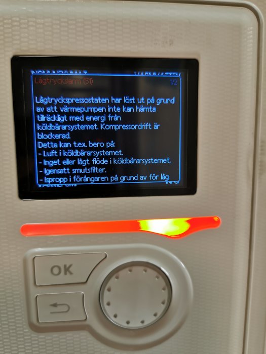 Kontrollpanel för värmepump med larmdisplay som visar ett lågtryckslarm och beskrivande feltext.