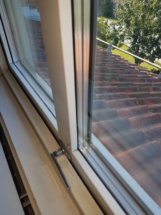 Utsikt från ett fönster högt upp, med fokus på en öppen fönsterluftlist och en närliggande takkant.
