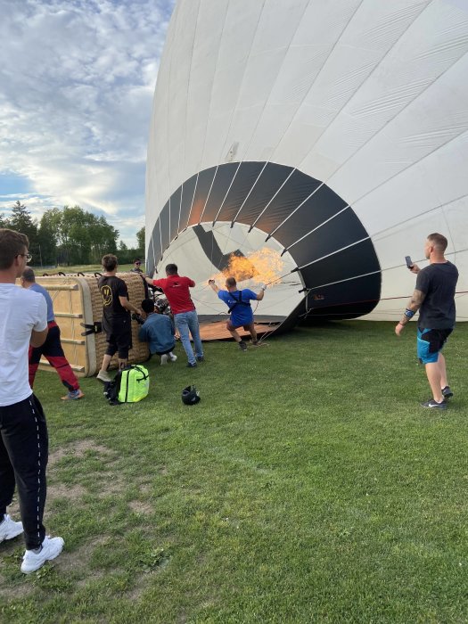 Personer som förbereder en hetluftsballong för flygning, med synlig eld vid ballongens öppning.
