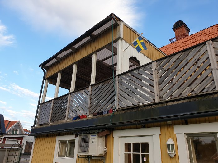 Gammalt uterum ovanpå garage med synlig skada och en svensk flagga, behöver renoveras.