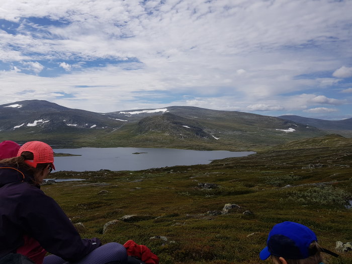 Personer tar en paus under en vandring med utsikt över en fjällsjö och karga högfjäll nära norska gränsen.