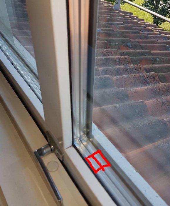 Vy inuti genom ett fönster som visar isolerkasetten och en tegeltakbakgrund, med ett rött markerat område.