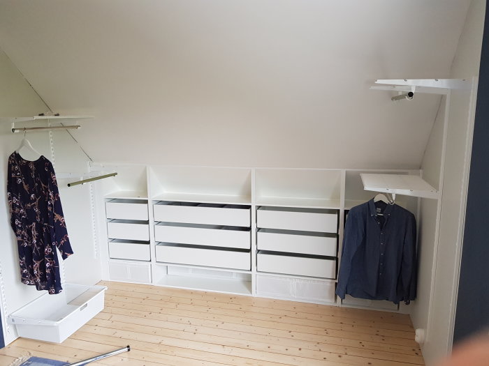 Custom-built wedge-shaped wardrobe with IKEA drawers and Elfa shelves under a sloped ceiling.